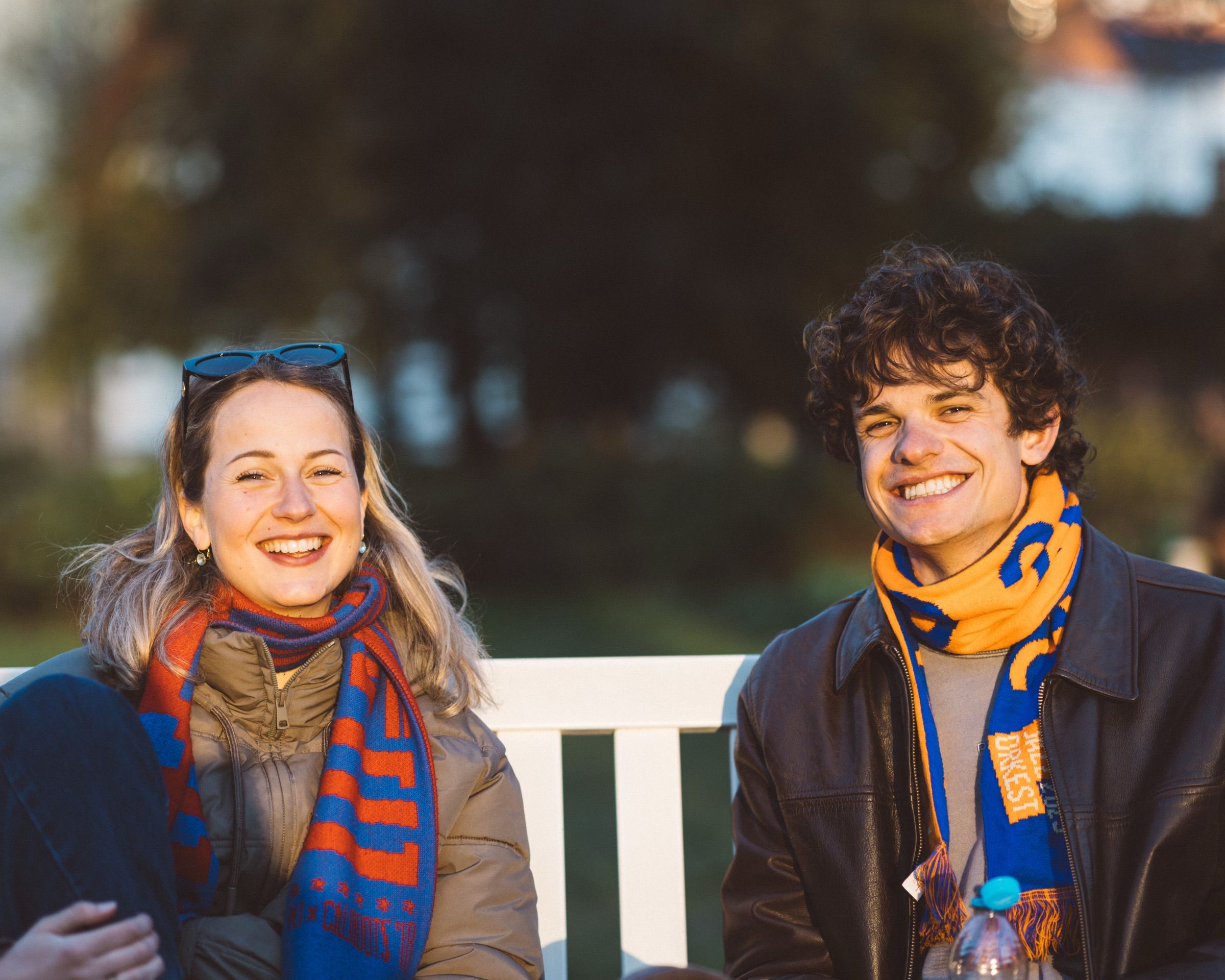 A woman and a young man in striped scarves laugh on a white park bench.