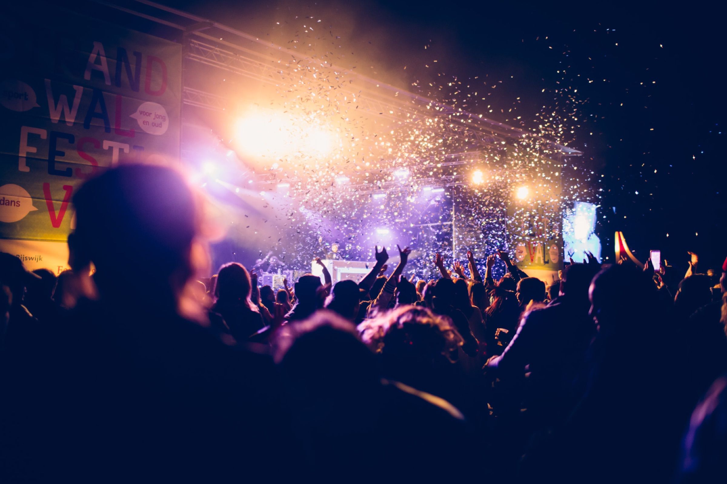A night crowd faces a festival stage as confetti bursts through the stage lights.