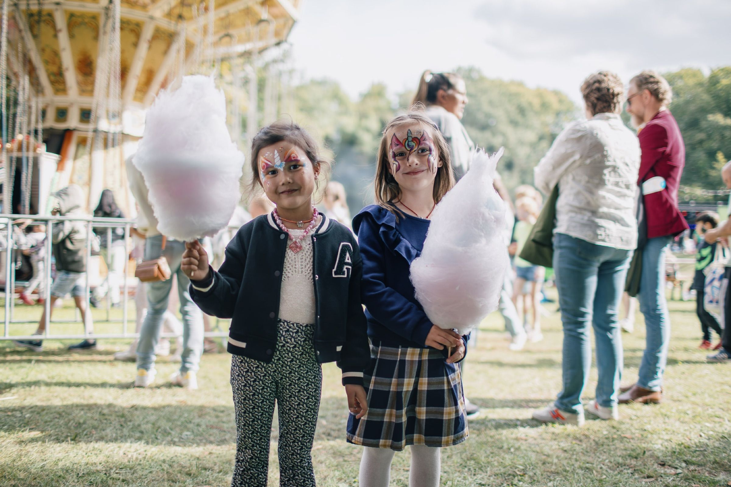 Two children hold huge clouds of pink candyfloss at a funfair.