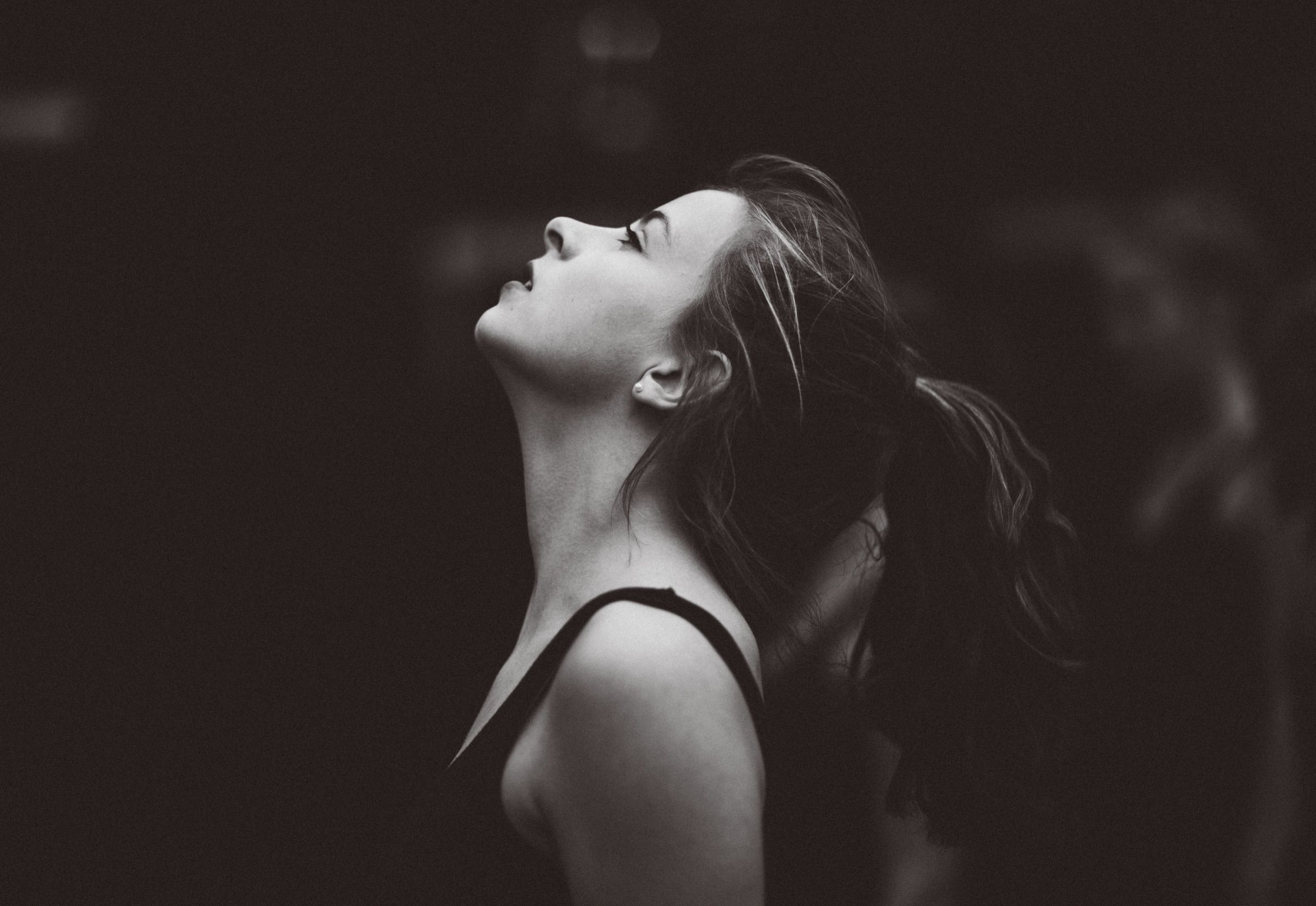 Black and white: a young dancer in profile tilts her face up into soft light against a dark background.