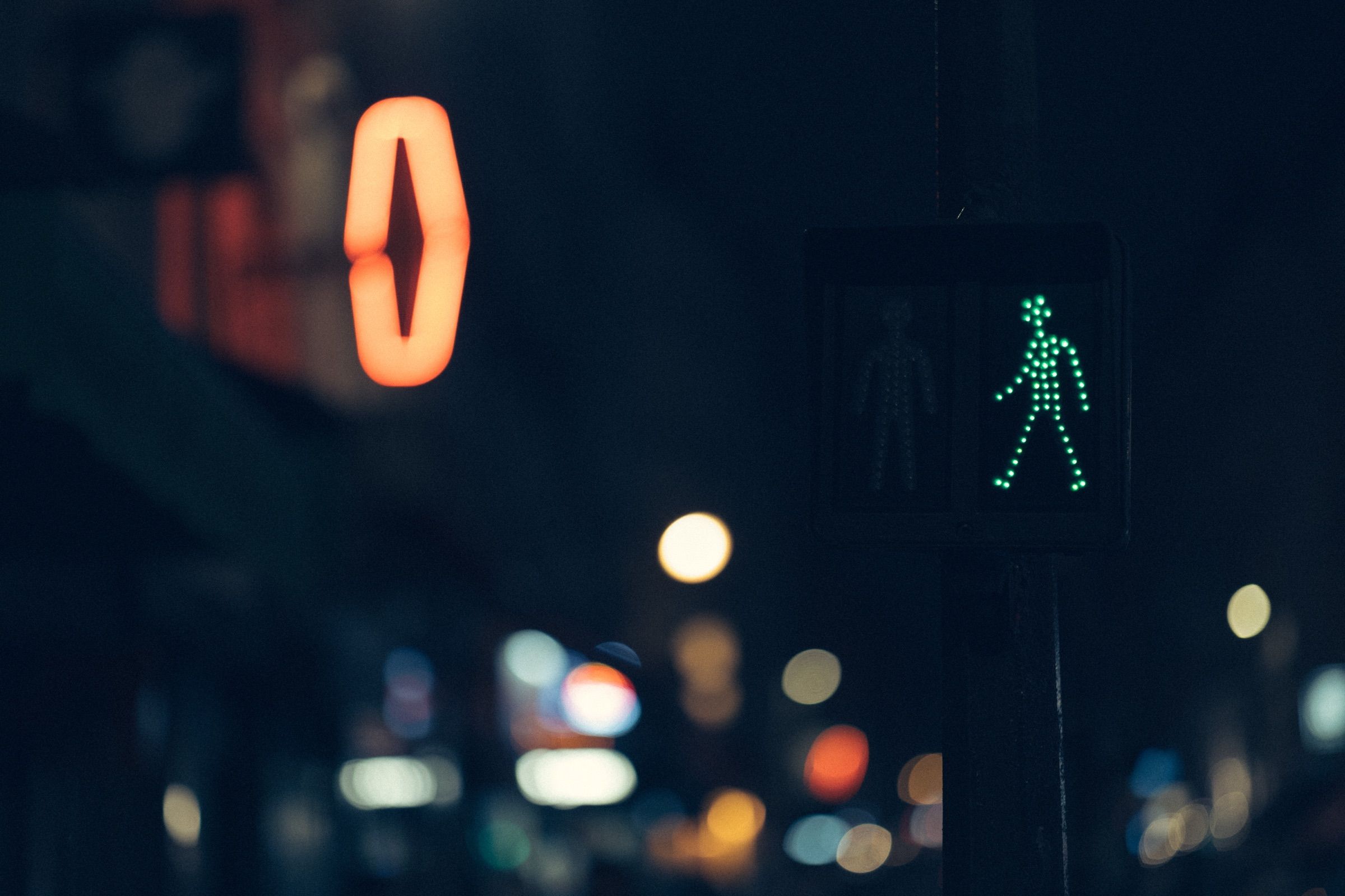 At night, a green walking-figure light glows among out-of-focus street lights.