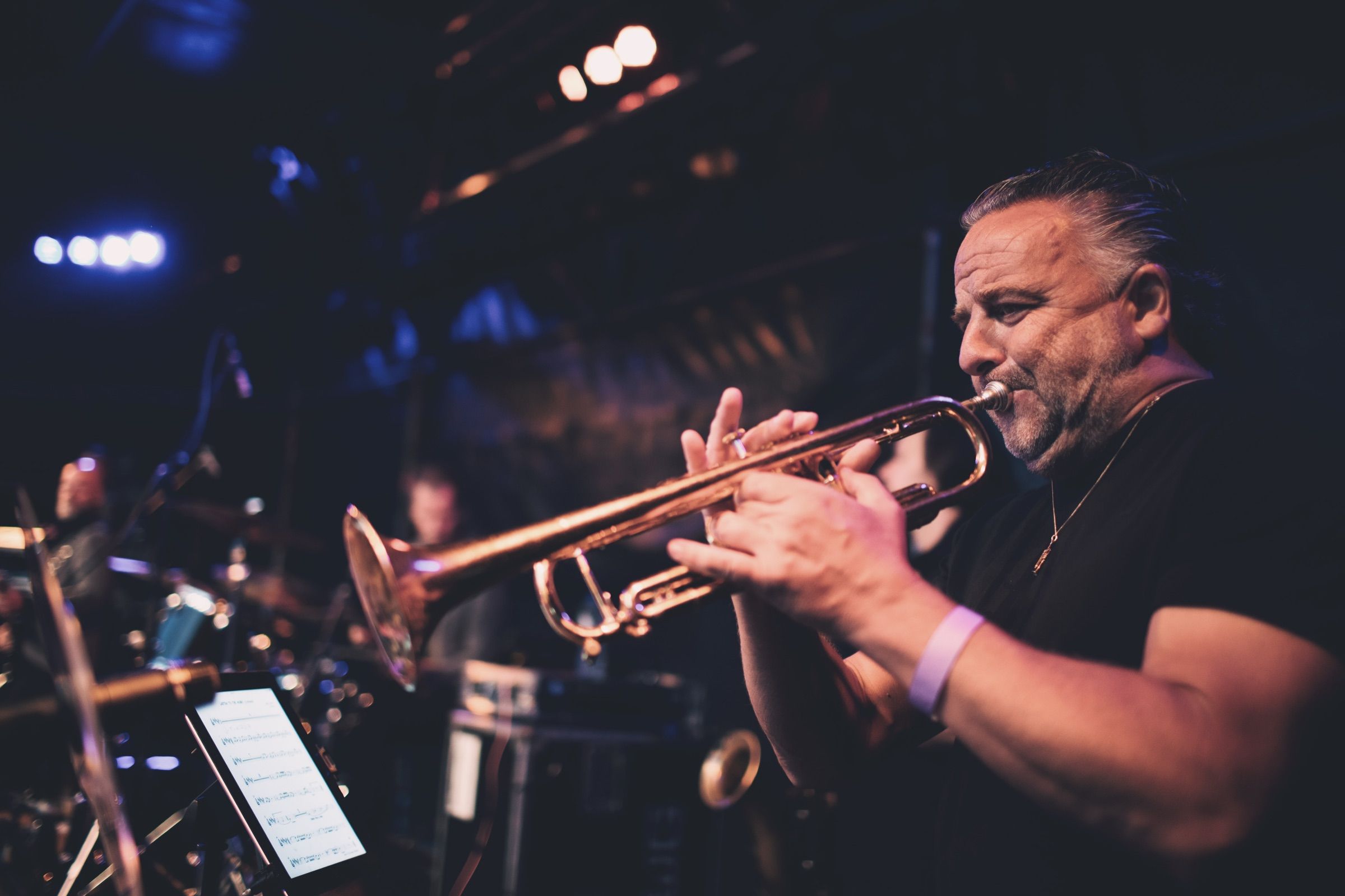 A trumpet player blows hard under blue and purple stage lights, the band behind him.