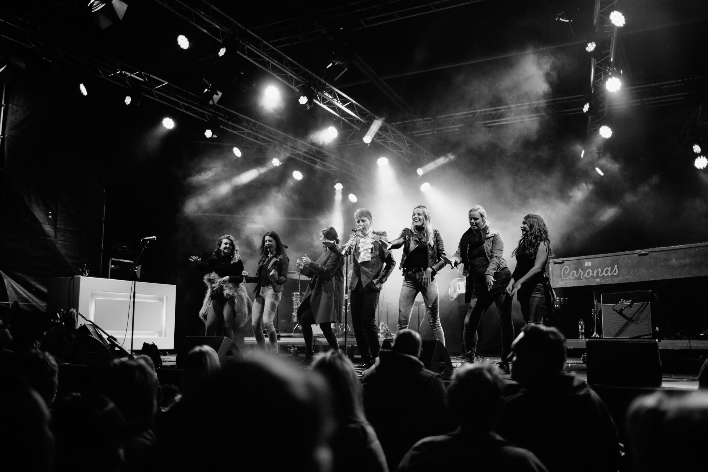 Black and white: a band performs under a rig of spotlights, the audience silhouetted in front.