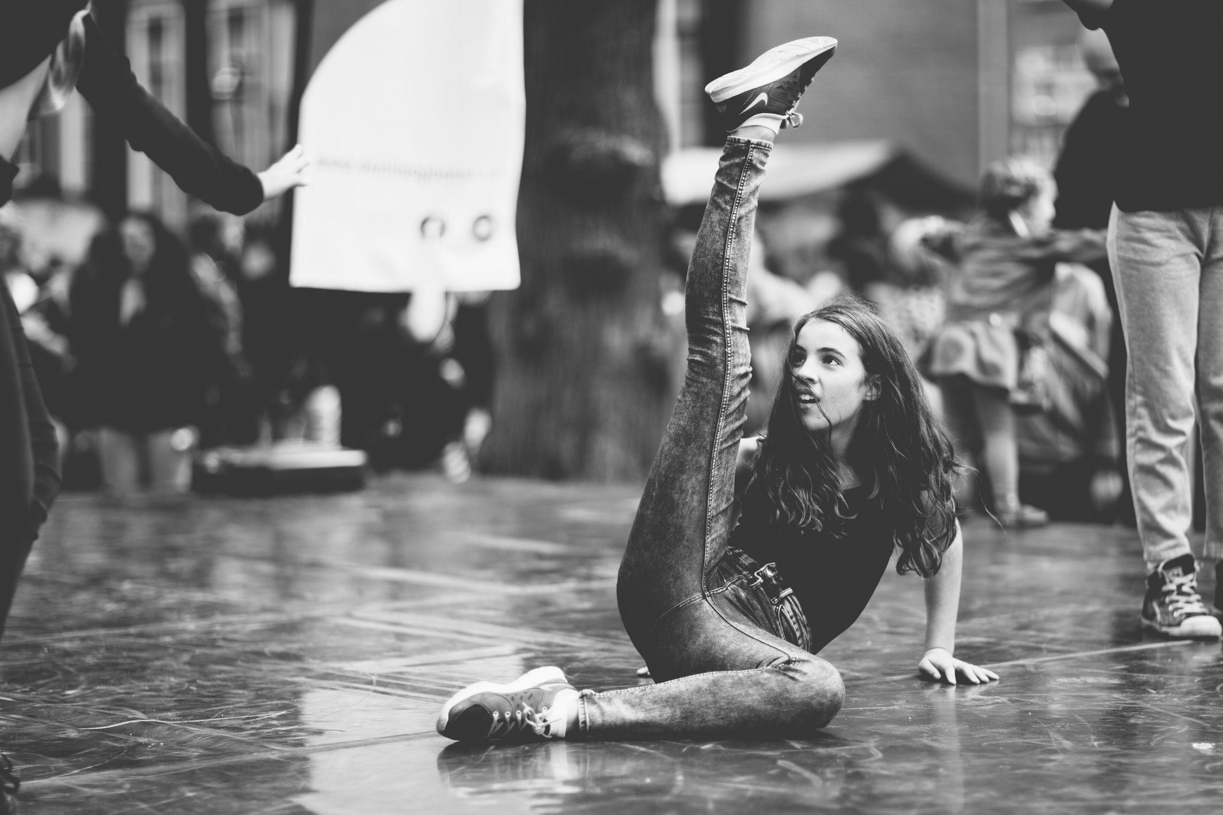 Black and white: a street dancer balances on one hand and kicks a leg high while people watch.