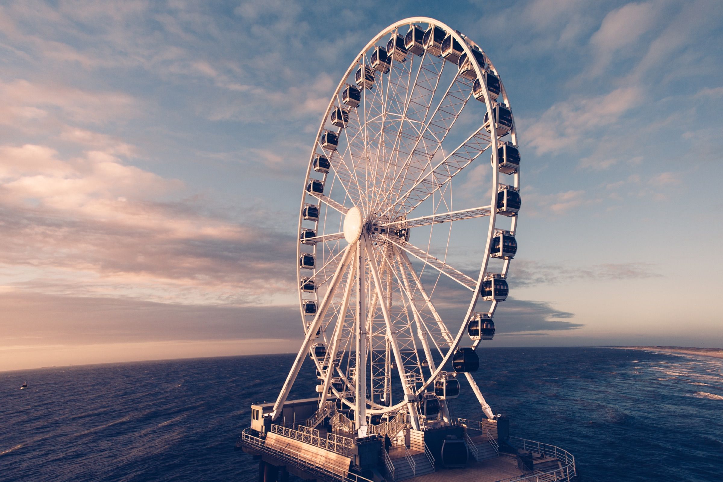 Een reuzenrad op een pier tegen een schemerlucht boven zee.